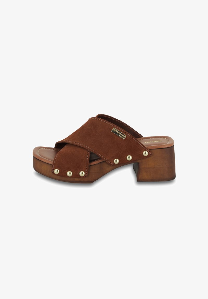 Sandale à talon en suède brun avec des brides croisées, talon en bois et accents en clous dorés. Semelle intérieure lisse. Conçue pour un confort optimal.