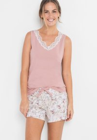 Débardeur rose pâle avec un col en dentelle festonné, associé à un short à motif floral avec un détail de noeud à la taille.
