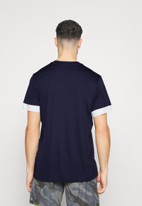 Camisa de manga corta de color azul marino con un cuello redondo y puños blancos en contraste. La tela parece suave; sin patrones ni logotipos visibles.