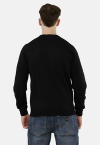 Maglione nero a maniche lunghe con collo a giro in un tessuto morbido, con maniche inserite e polsini a coste. Abbinato a jeans blu, vista da dietro.