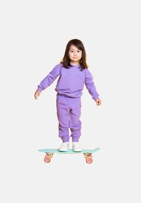 Fioletowa bluza i dresy noszone przez dziecko, stojące na turkusowej desce skateboardowej z różowymi kołami, na białym tle.