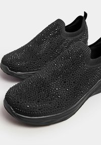 Chaussures noires à enfiler avec une tige en tissu texturé ornée de strass dispersés, et une semelle en caoutchouc flexible et texturée.