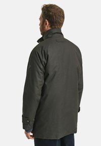 Donkergroen, middellang jasje met een hoge kraag, knoopsluiting bij de mouwen en een zachte textuur. Heeft een gedetailleerd stikpatroon op de achterkant.