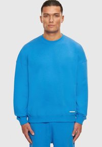 Blå bomullssweatshirt med rund hals, drop shoulders og ribbestrikkede mansjetter. Inkluderer en liten logoakzent på kanten.