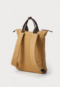 Canvas backpack with brown fabric, dual top handles, adjustable straps, and a zippered closure. Features minimal stitching detail.
