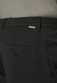 Svarta skräddarsydda byxor med en slät yta, med en bakficka, knäppning med knapp och en liten "Icebreaker"-tagg synlig på midjan.