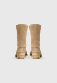 Bottines en daim beige jusqu'au genou avec un bout arrondi et un talon bloc empilé. Dotées d'une fermeture éclair à l'arrière pour un enfilage facile. Texture lisse.