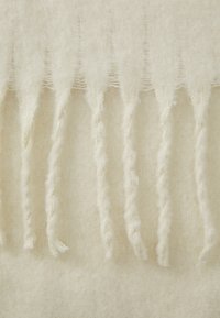 Beige uldslå med frynser på kanterne, der har en blød tekstur og snoede garn detaljer, hvilket skaber et hyggeligt og varmt udseende.