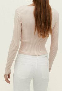 Langärmliges, geripptes Oberteil in Hellrosa, kombiniert mit weißen, hoch taillierten Jeans. Verfügt über ein figurbetontes Design und strukturiertes Strickmaterial mit dezenten Nahtdetails.