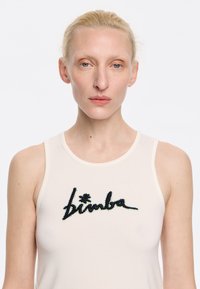 Kreemjas värvuses ilma varrukateta särk, millel on must tikandiga "bimba" logo ning värvikad aktsendid. Üksikasjalik, sujuv kangas, mis on sobivalt kujundatud.