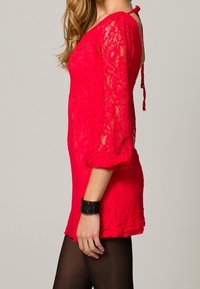 Robe en dentelle rouge à manches trois-quarts, coupe ajustée et dos ouvert. Texturée avec des motifs floraux, assortie d'un bracelet noir.