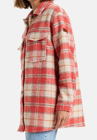 Rotes und cremfarbenes kariertes Flanellhemd-Jacke mit zwei Brusttaschen, Knopfverschluss und strukturiertem Stoff. Mit braunem Akzentetikett am Ärmel.