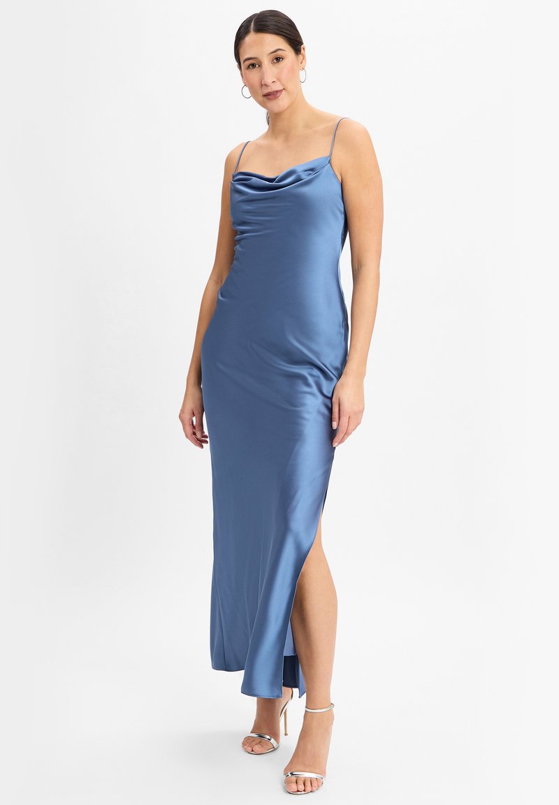 Satin blaues Maxikleid mit einem gerafften Ausschnitt, dünnen Trägern und einem Seitenschlitz. Der Stoff hat eine glatte, glänzende Oberfläche. Ergänzt durch silberne Absätze.