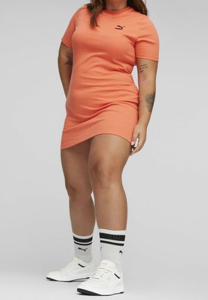Robe côtelée à manches courtes de couleur orange vif avec un col rond et un logo discret. Associée à des baskets blanches et des chaussettes rayées.