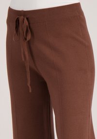 Bruine gebreide joggers met een taillekoord, voorzien van een gladde textuur en zijnaden, ontworpen voor comfort en casual gebruik.