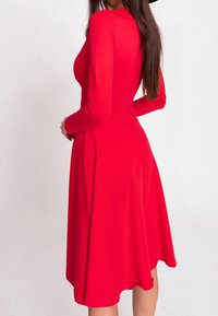 Robe longue rouge à manches longues avec un corsage ajusté et une jupe fluide. Fabriquée dans un tissu lisse et extensible. Aucune motif ou ornement visible.