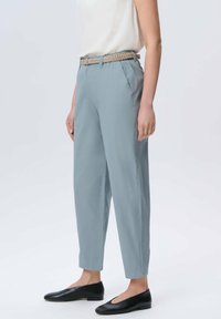 Jasnoniebieskie, zwężane spodnie z plecionym beżowym paskiem, o gładkiej fakturze i przednich kieszeniach, w połączeniu z czarnymi butami wsuwanymi.