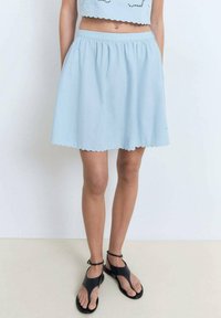 Falda de color azul claro, hasta la rodilla, con una cintura fruncida y dobladillo en forma de ondas. Hecha de una tela suave, presenta una textura lisa sin patrones visibles.