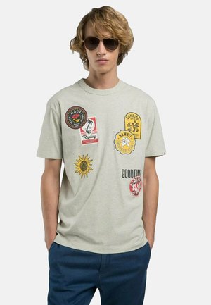 T-shirt in cotone grigio con vari patch colorati, tra cui disegni di sole e palma, sulla parte frontale. Maniche corte, collo a giro.