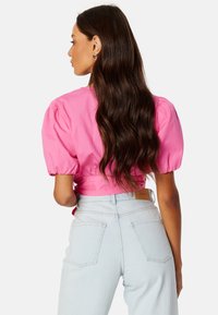 Blusa corta rosa con maniche a sbuffo, abbinata a jeans azzurri a vita alta. L'outfit presenta una texture sottile e un design aderente.