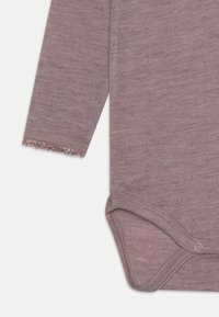 Ilgomis rankovėmis mauve spalvos kūdikio bodis, pagamintas iš minkštos mezgimo medžiagos, su tekstūruotu raštu ir snapsų uždarymu apačioje, kad būtų lengva apsirengti.