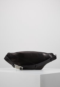 Borsa in pelle nera con una texture morbida, forma slim e tracolla regolabile. Presenta una fibbia in metallo argento per una chiusura sicura.