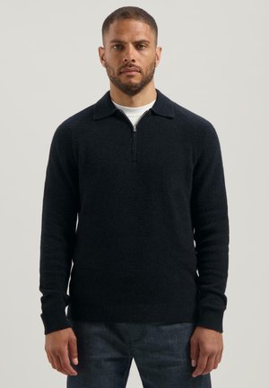 Marineblauwe pullover trui met een ritskraag, geribbelde manchetten en tailleband, voorzien van een gestructureerde stof en een getailleerd ontwerp.