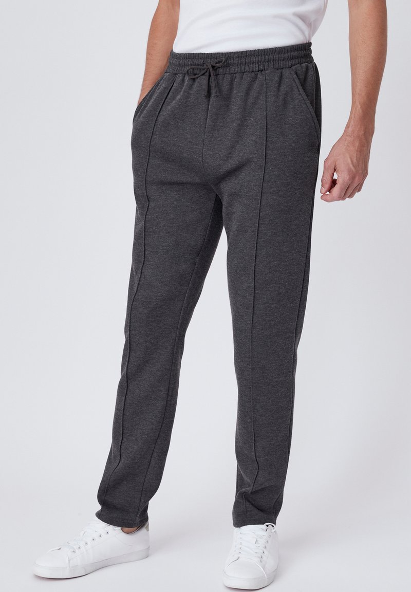 Donkergrijze joggingsbroek van zacht materiaal, met een elastische tailleband, trekkoordsluiting, zijzakken en contrasterende zijnaad.