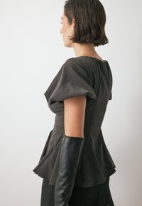 Dunkelgraues Peplum-Oberteil mit kurzen Puffärmeln. Aus strukturiertem Stoff gefertigt, mit einem taillierten Oberteil und einem schwingenden Saum. Begleitet von langen schwarzen Handschuhen.
