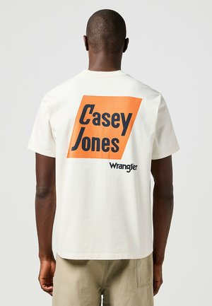 Witte katoenen t-shirt met een rechthoekige oranje graphic met de tekst "Casey Jones" in vette zwarte letters en het "Wrangler"-logo eronder.