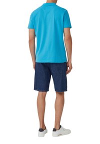 Turkusowa koszulka polo, krótki rękaw, materiał bawełniany. Połączona z ciemnymi dżinsowymi szortami, do kolan, prosty design. Białe sneakersy z granatowymi akcentami.