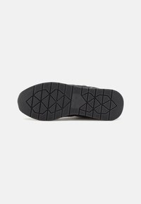 Suola di scarpa in gomma nera con un motivo di battistrada testurizzato, caratterizzata da un logo centrale e forme esagonali per una migliore aderenza. Materiale liscio e durevole.