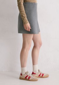 Grauer gestrickter Minirock mit ausgestellter Silhouette, kombiniert mit beigen und roten Sneakern sowie cremefarbenen Socken, vor einem schlichten Hintergrund präsentiert.