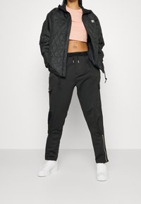 Black quilted jacket, pale pink cropped top, and black cargo pants with zippers. White sneakers complete the outfit.