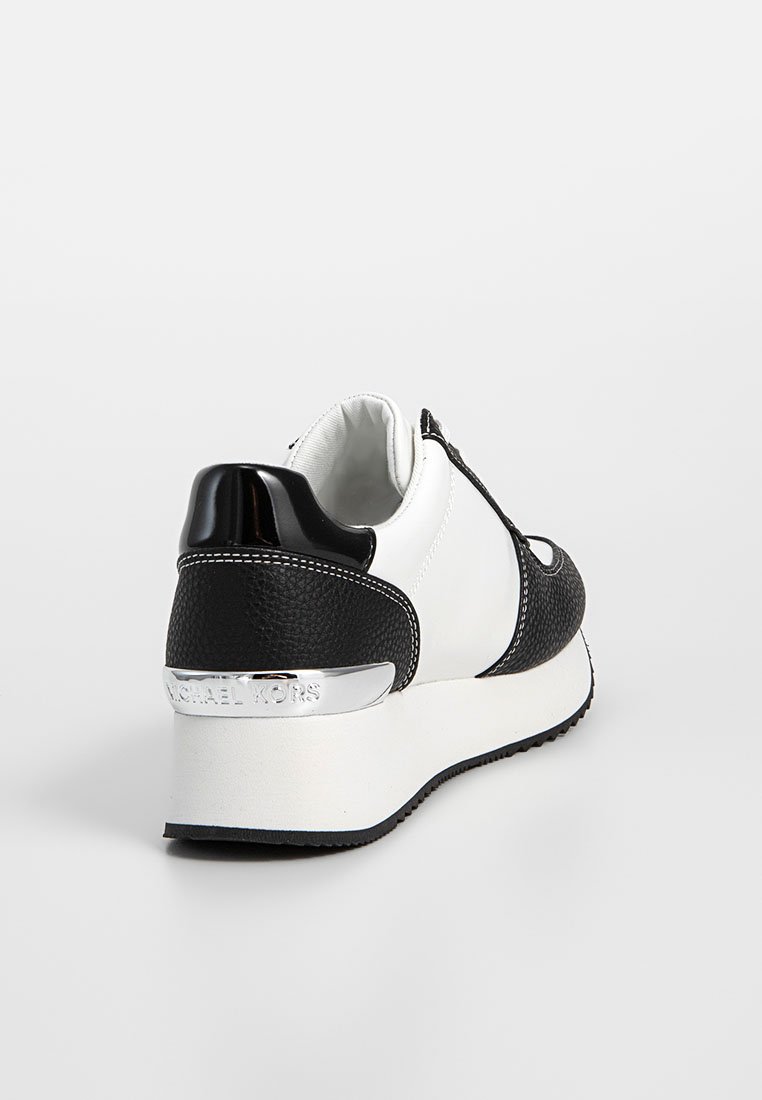 Baskets blanches et noires avec des accents en cuir et texturés, dotées d'un capuchon de talon noir brillant et d'une plaque logo métallique au niveau du talon.