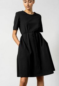 Schwarzes Kurzarmkleid aus weichem Stoff, mit Taillengürtel und seitlichen Taschen; A-Linien-Silhouette mit lässiger Passform.