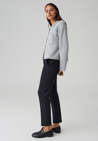 Cardigan grigio a coste con taschino sul petto, abbinato a pantaloni neri a gamba stretta e mocassini neri. Design semplice e minimalista.