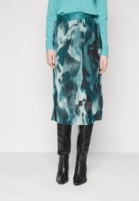 Jupe midi plissée en motif abstrait bleu canard et noir, fabriquée en tissu texturé. Associée à des bottes en cuir noir montant jusqu'aux genoux.