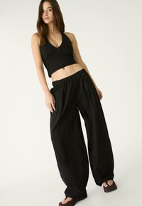 Schwarzes, kurz geschnittenes Tanktop kombiniert mit lockeren schwarzen Hosen. Die Hose hat einen elastischen Bund und ein weites Bein. Glatte Textur, minimalistischer Stil.