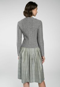Grau gestrickter Pullover mit einem strukturierten Rautenmuster, kombiniert mit einem knielangen, hellgrünen Rock mit einem wirbelnden Design.