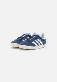 Marineblauwe suède sneakers met witte lederen strepen, rubberen zool en blauwe logo-tag op de tong. Klassiek lichtgewicht laag model.