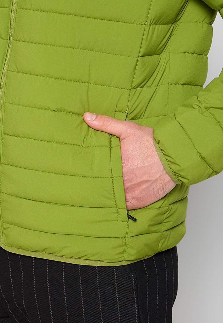 Giacca imbottita verde con chiusura a zip, caratterizzata da trapuntatura orizzontale, una tasca laterale e polsini elasticizzati, mostrata su una mano che tiene la tasca.