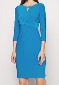 Tealfärgad klänning med långa ärmar och en figurnära passform. Har en draperad front och en nyckelhålsöppning vid halsen. Slät tygstruktur.