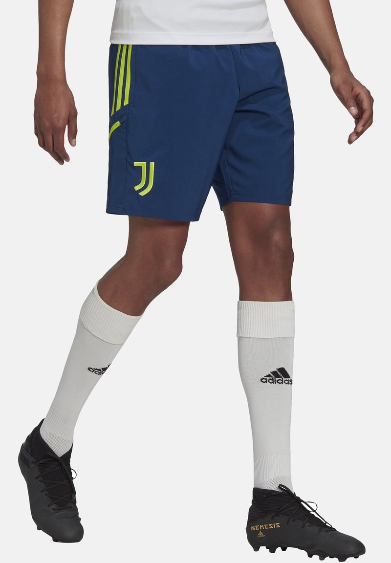 Personne portant un short bleu Juventus, des chaussettes blanches Adidas montantes et des crampons noirs Adidas Nemesis.