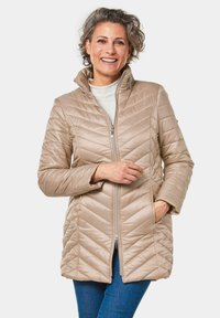 Beige gewatteerde jas met een hoge kraag, met diagonale stiksels. Ritsluiting en zijzakken. Draag met een licht overhemd, gecombineerd met denim.