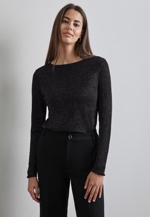 Top nero a maniche lunghe con una leggera lucentezza, scollo a barca e polsini scallopati, abbinato a pantaloni neri a vita alta.