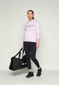 Felpa leggera rosa con logo "Champion" blu, leggings neri, scarpe da ginnastica nere e borsa a tracolla nera. Tessuto morbido, design atletico casual.