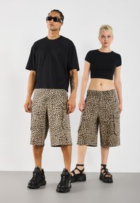 Melnas oversize T-krekls, leopardu raksta kravas šorts un melnas masīvas kurpes. Šortiem ir lielas sānu kabatas un brīvs piegriezums.