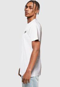 White cotton t-shirt with short sleeves, featuring a small black logo on the chest and a relaxed fit. Smooth texture, crew neckline.