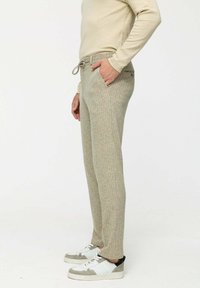 Könnyű, mintás jogger nadrág bézs és zöld színkombinációban, elasztikus derékkal és oldalsó zsebekkel, fehér sportcipővel párosítva.